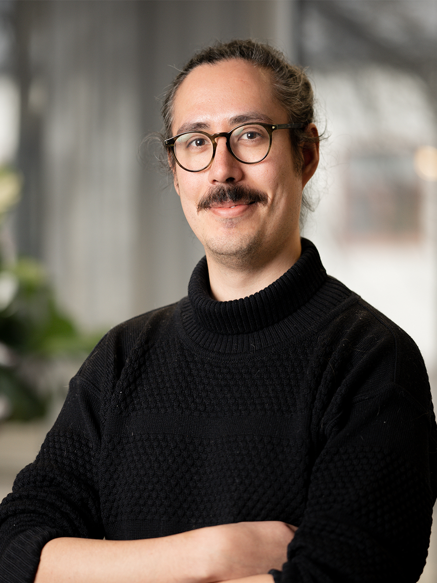A person standing with arms crossed against a softly blurred indoor background.